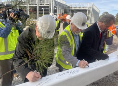 Three men in hard hats sign a steel beam at a construction site.