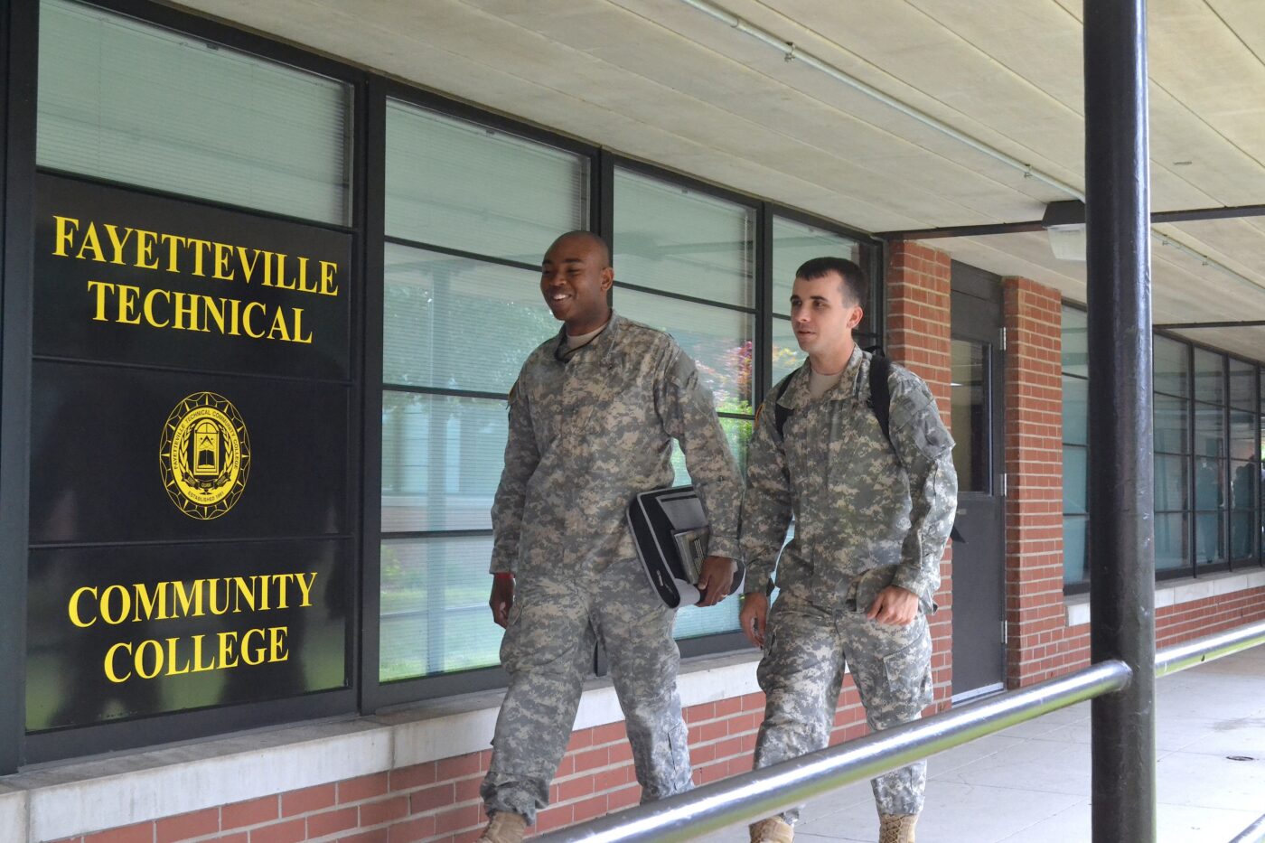 Two men dressed in military uniforms walk in front of a Fayetteville Tech building.