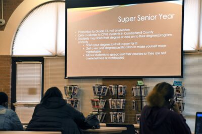 Two people face a screen displaying information about Super Senior Year at Cumberland Polytechnic High School