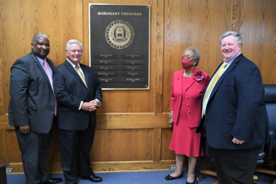 Glenn Adams, Larry Keen, Marye Jeffries and David Williford stand in front of a wall-mounted plaque with the names of the College's Honorary Trustees on it.