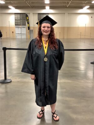 A graduate with long red hair stands smiling at the camera.