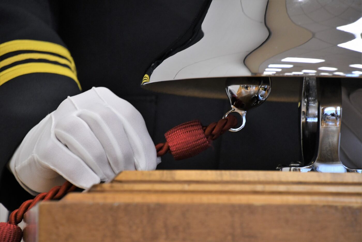 Close up photo a hand in a white dress glove holding a red rope tied to the ringer of a silver bell.