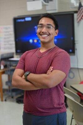 Luis Mancilla, a 17-year-old boy with dark hair and glasses, stands with his arms crossed smiling at the camera.