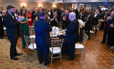 A room full of people in formal attire stand and applaud Dr. Larry Keen, who is standing in the foreground.