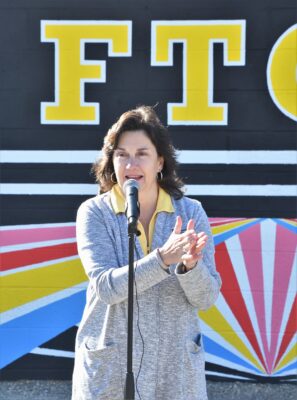 Sandy Ammons claps her hands while speaking into a microphone in front of the FTCC Success Closet.