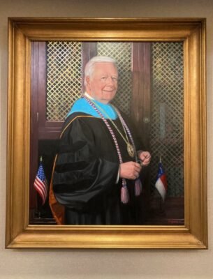 A framed oil painting portrait of Dr. Larry Keen in academic regalia.
