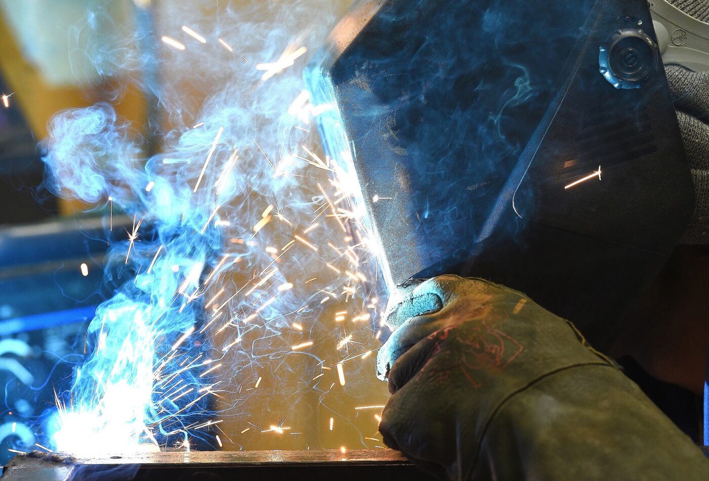 A close-up photo of a person wearing protective helmet and gloves welding metal.