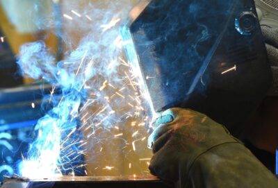 A close-up photo of a person wearing protective helmet and gloves welding metal.