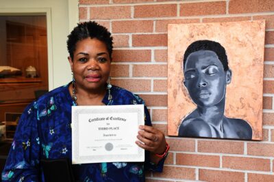 Jacquelyn D. Forrest stands by her artwork, "La Femme Natorelle" and holds her third place certificate.