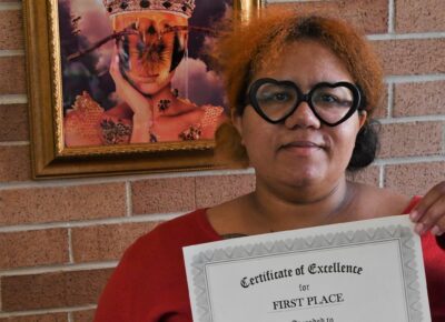 Tesia Dresser stands in front of her artwork and hold her first place certificate.