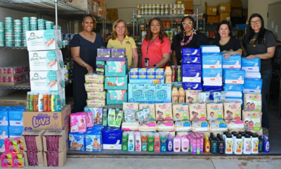 A group of women standing behind stack of personal items in a food pantry.