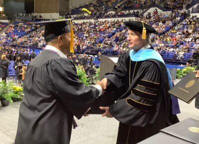 FTCC President Dr. Mark Sorrells shakes hands with a graduate while handing him a diploma folder.