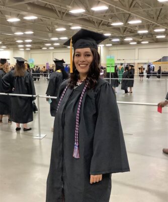 A graduate in a cap and gown with a red, white and blue cord poses for the camera