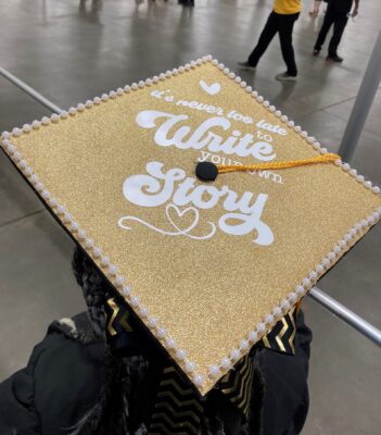 Graduation cap decorated with a gold background and white lettering that says it's never too late to write your own story.