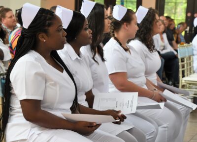 Graduates of the Practical Nursing program sit in a row. They are dressed in white uniforms with caps.