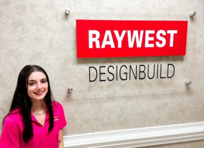 Whitney Carter stands by a logo that says Ray West Design Build
