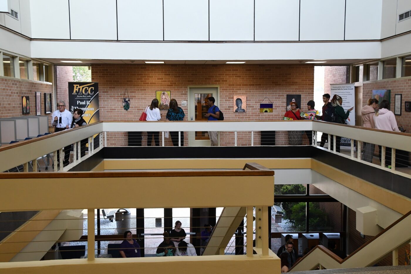A wide photo showing people walking around the top floor of the library looking at artwork on the walls.