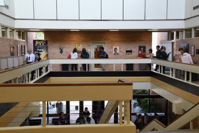 A wide photo showing people walking around the top floor of the library looking at artwork on the walls.