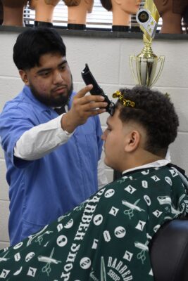 Barbering student Danny Garcia uses clippers on a client's hairline.