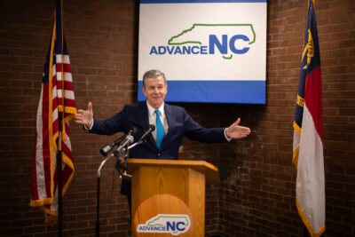 Gov. Roy Cooper stands behind a podium with his hands spread wide.