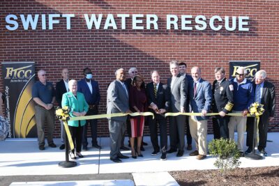 A group of people cut a ribbon in front of a brick building that has Swift Water Rescue written on it.