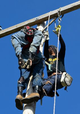 A student in lineworker gear practices saving a dummy that is stranded on an electric pole.