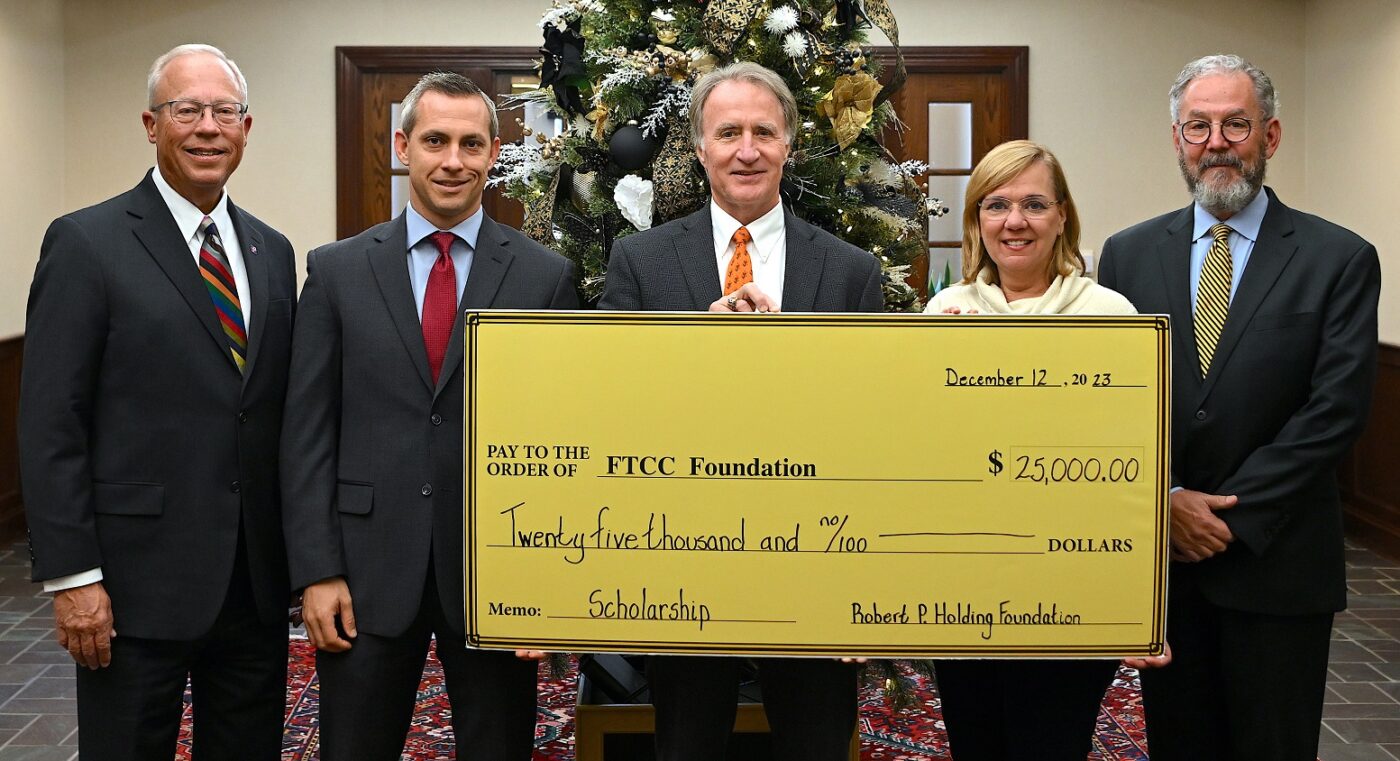Four men and one woman stand while holding a large presentation check.