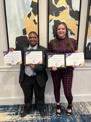 Two students stand holding award certificates.