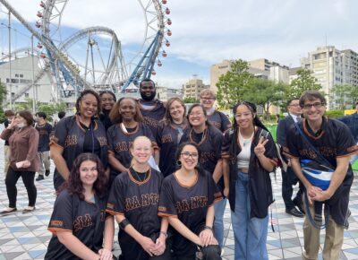 A group of people wearing baseball jerseys stands in front of a roller coaster