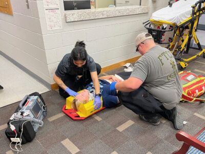 Two EMS students strap a student pretending to be a patient to a backboard.