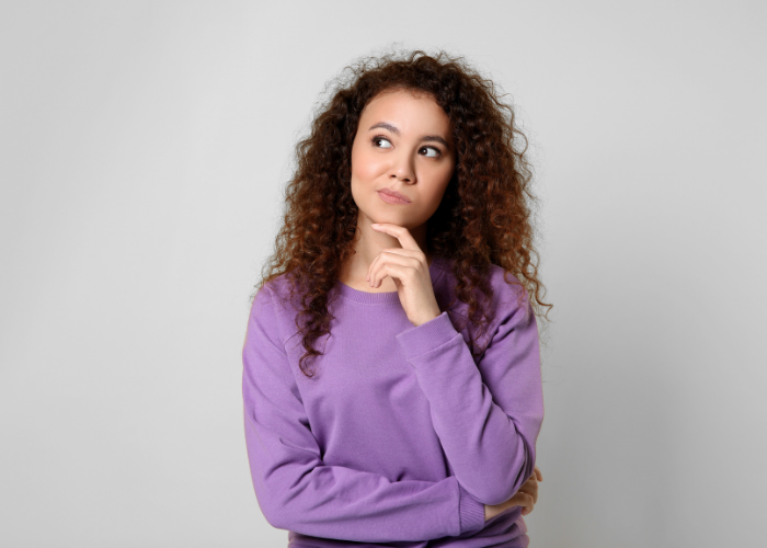 Curly-haired woman in a purple sweater resting her chin on her hand.