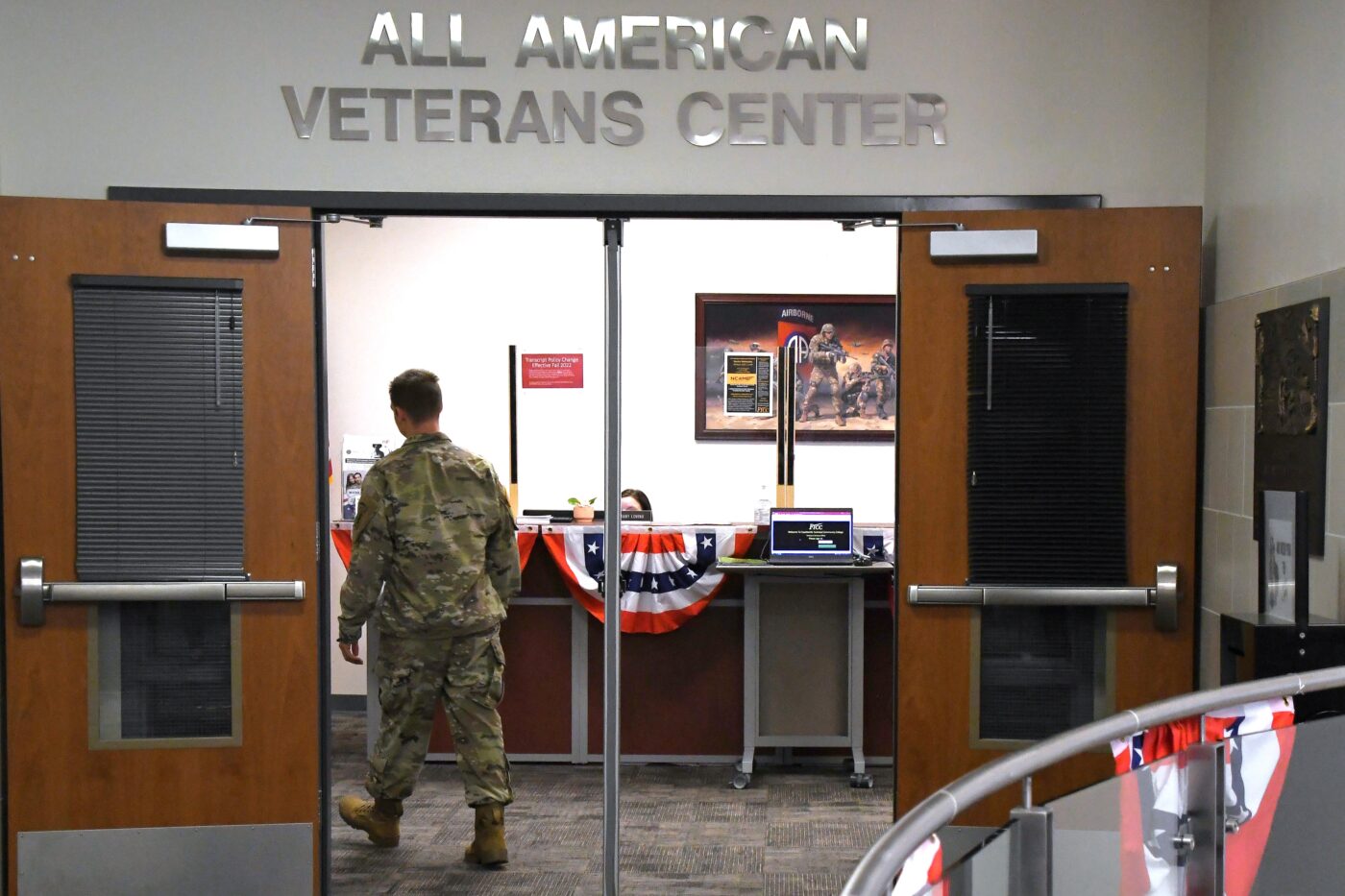A man in a military uniform walks through double doors under a sign that says All American Veterans Center