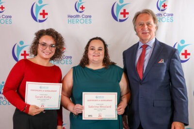 Two women holding certificates stand next to a man in a suit.