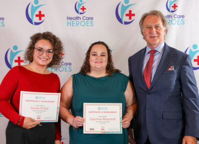 Two women holding certificates stand next to a man in a suit.