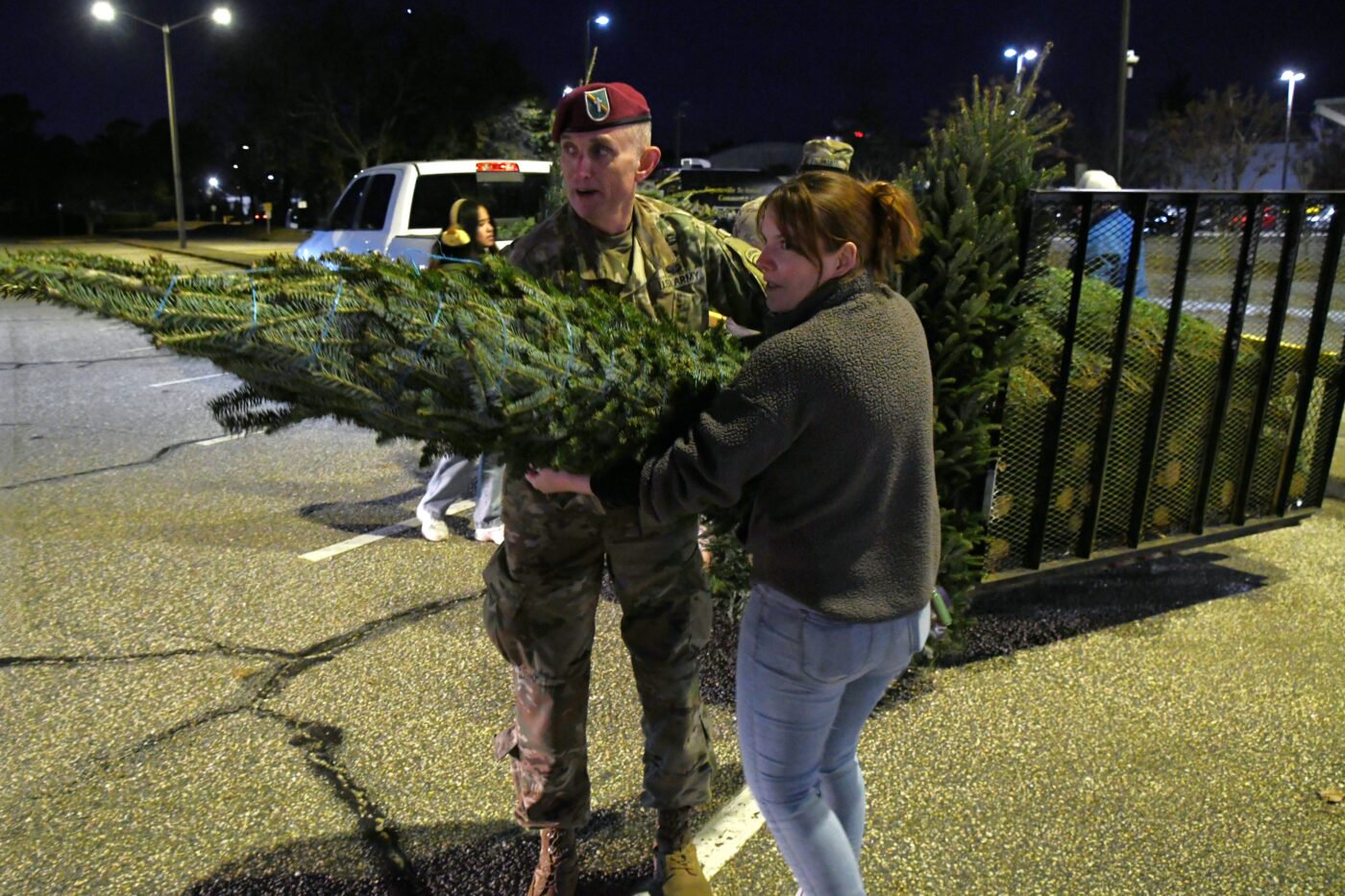 A man in a military uniform and a woman carry a Christmas tree.