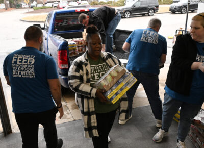 A group of people unload boxes of canned food off the bed of a pickup truck.