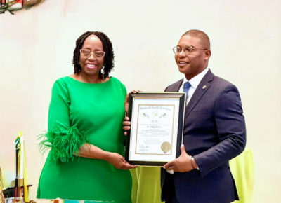 A woman in a green dress and a man in a suit pose with a framed certificate.