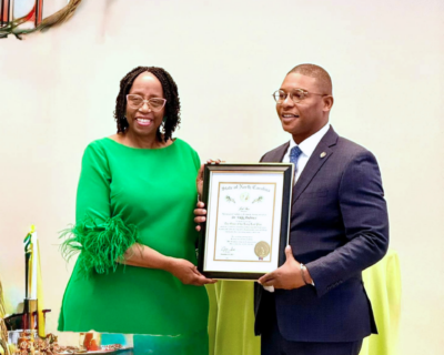 A woman in a green dress and a man in a suit pose with a framed certificate.