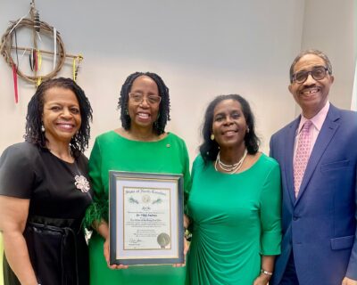 Three women and a man pose with a framed certificate.