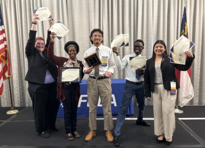 A group of students in business attire hold up certificates.