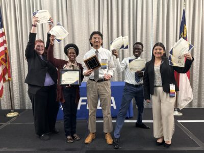 A group of students in business attire hold up certificates.