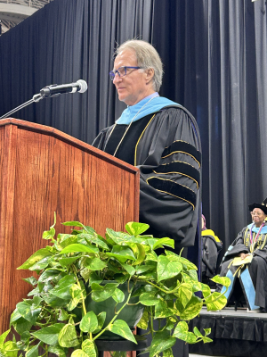 A man in doctoral regalia stands at a podium.