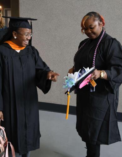 A-graduate-shows-off-her-decorated-cap-to-another-graduate-who-points-at-it-in-delight