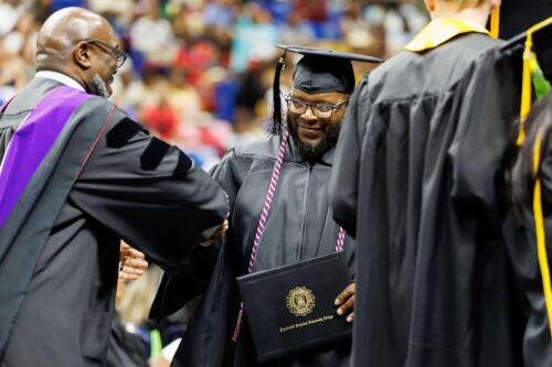 A-smiling-graduate-center-is-congratulated-with-a-handshake