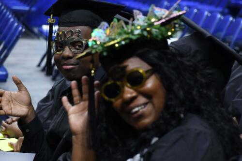 Two-graduates-both-wearing-decorative-glasses-wave-at-the-camera