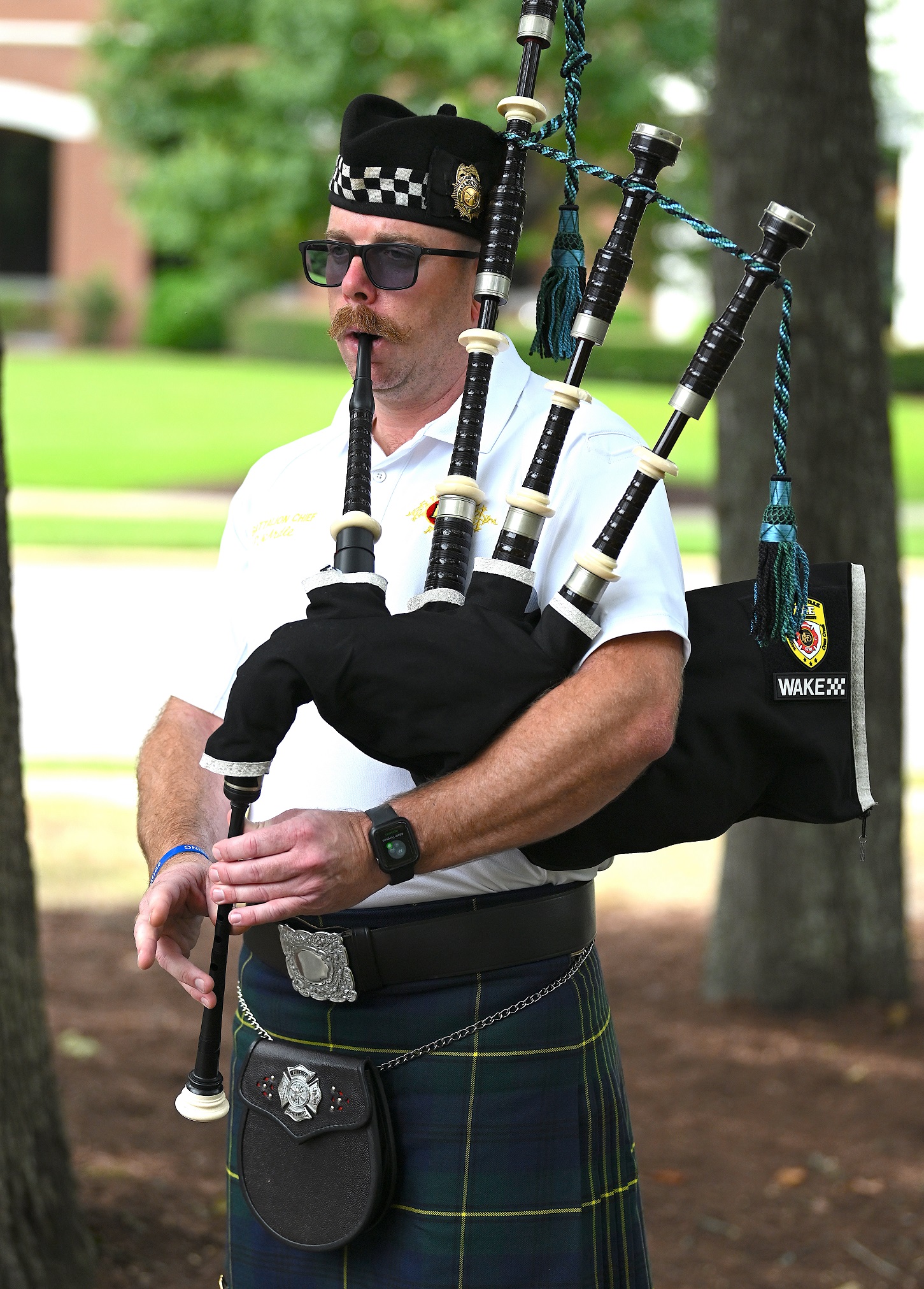A man wearing a kilt and sunglasses plays the bagpipes.