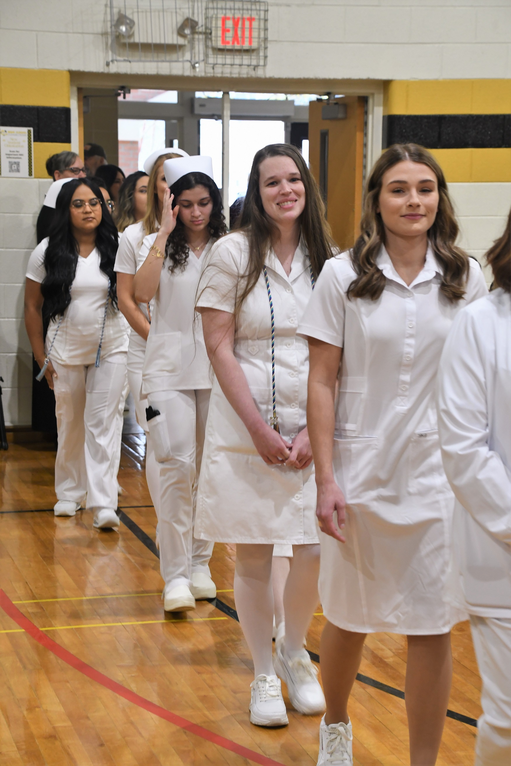 A line of ADN graduates walk in to the pinning ceremony. They are dressed in all white nursing uniforms.