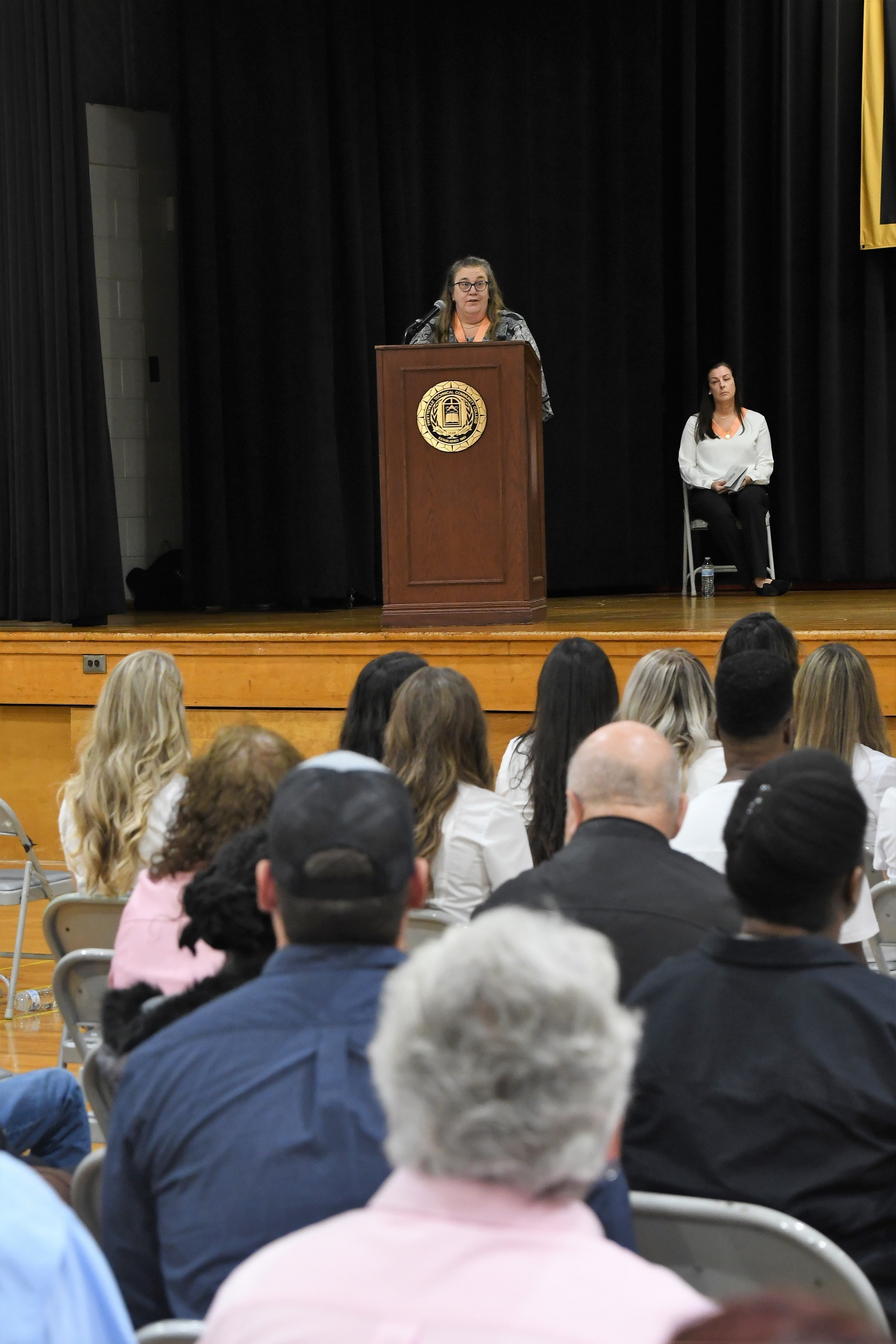 Dr. Sharon Gallagher is seen in the background standing behind the podium. The back of the audience is in the foreground.