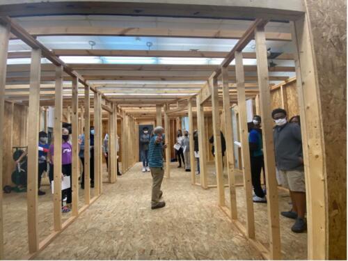 A group of students standing inside a striped construction learning room. 