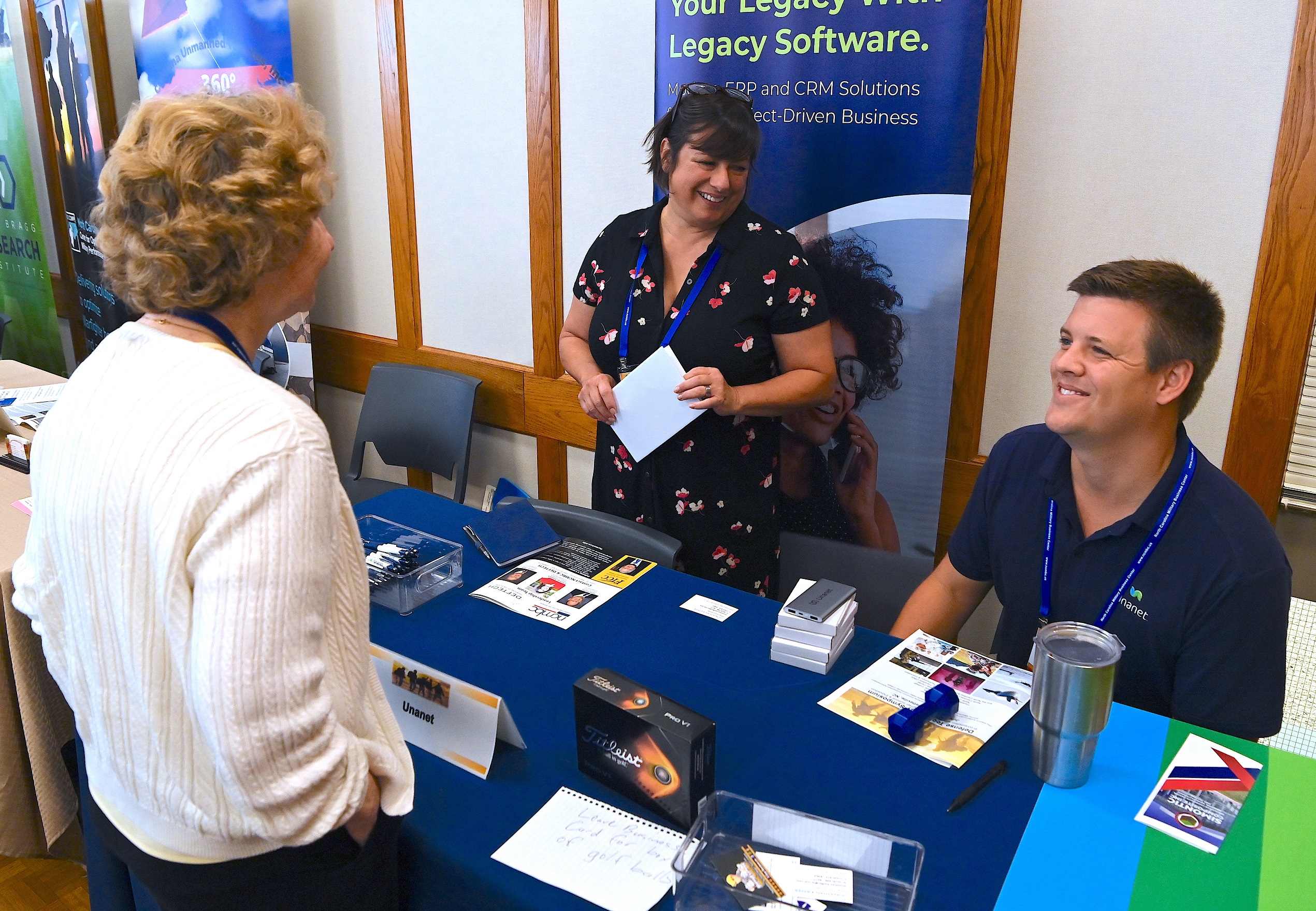 Vendors at the Defense Technology Symposium speak at a table.